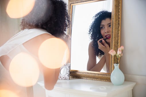 557475351-mixed-race-woman-applying-lipstick-in-mirror-gettyimages